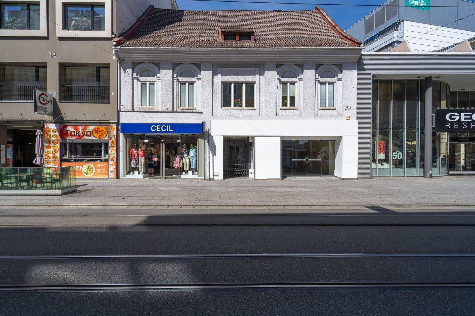 Historische Fassade eines Geschäftsgebäudes an einer belebten Straße mit modernen Ladenfronten.