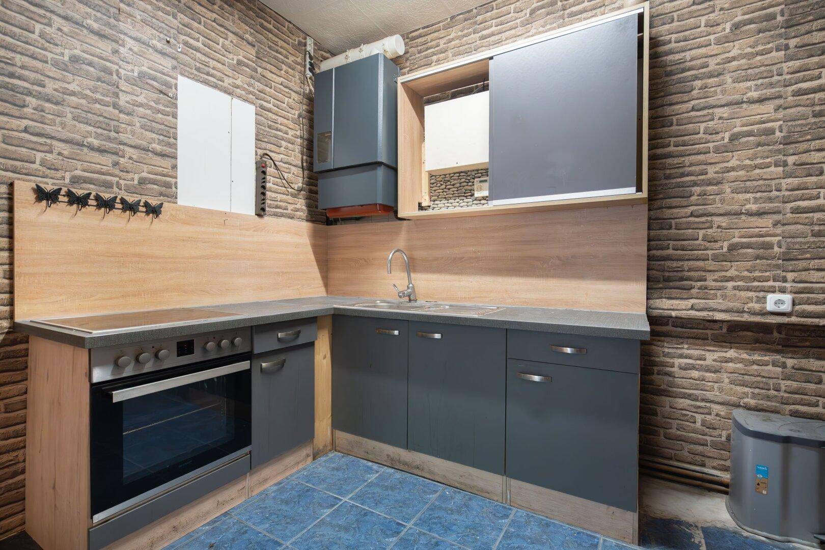 Funktionale Küchenzeile mit blauen Fliesen, grauen Schränken und Backofen in rustikalem Ambiente.