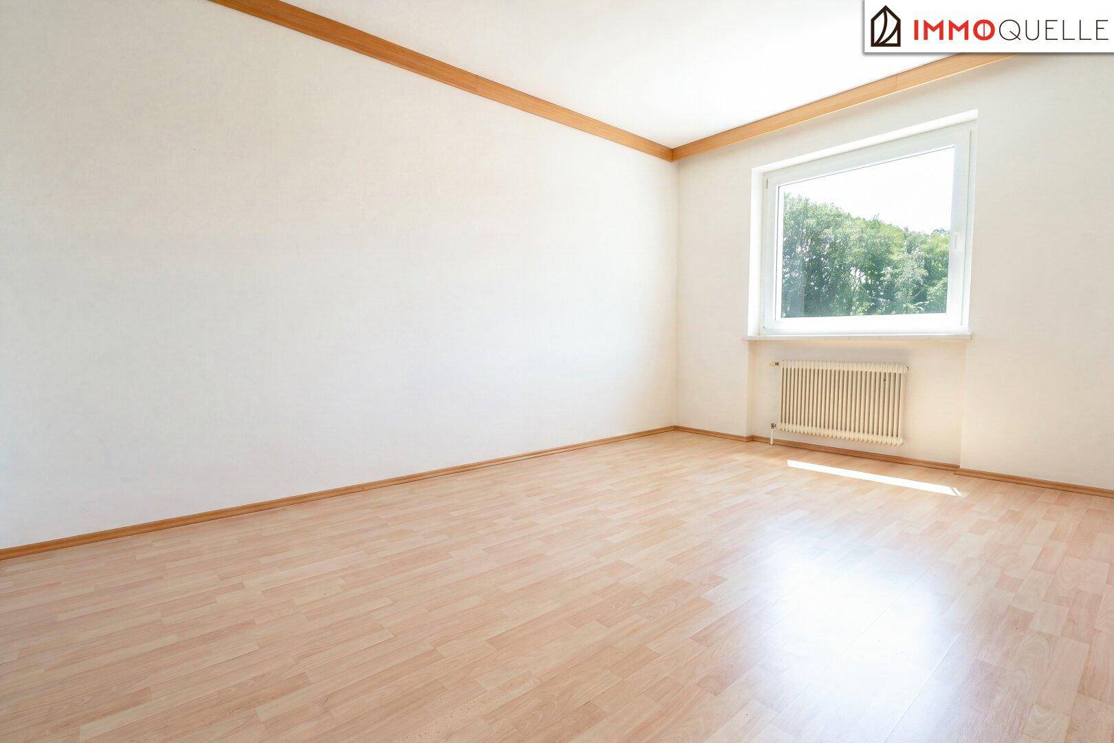 Leeres Schlafzimmer mit Holzboden, Fenster und Holzleiste an der Decke, hell und geräumig.