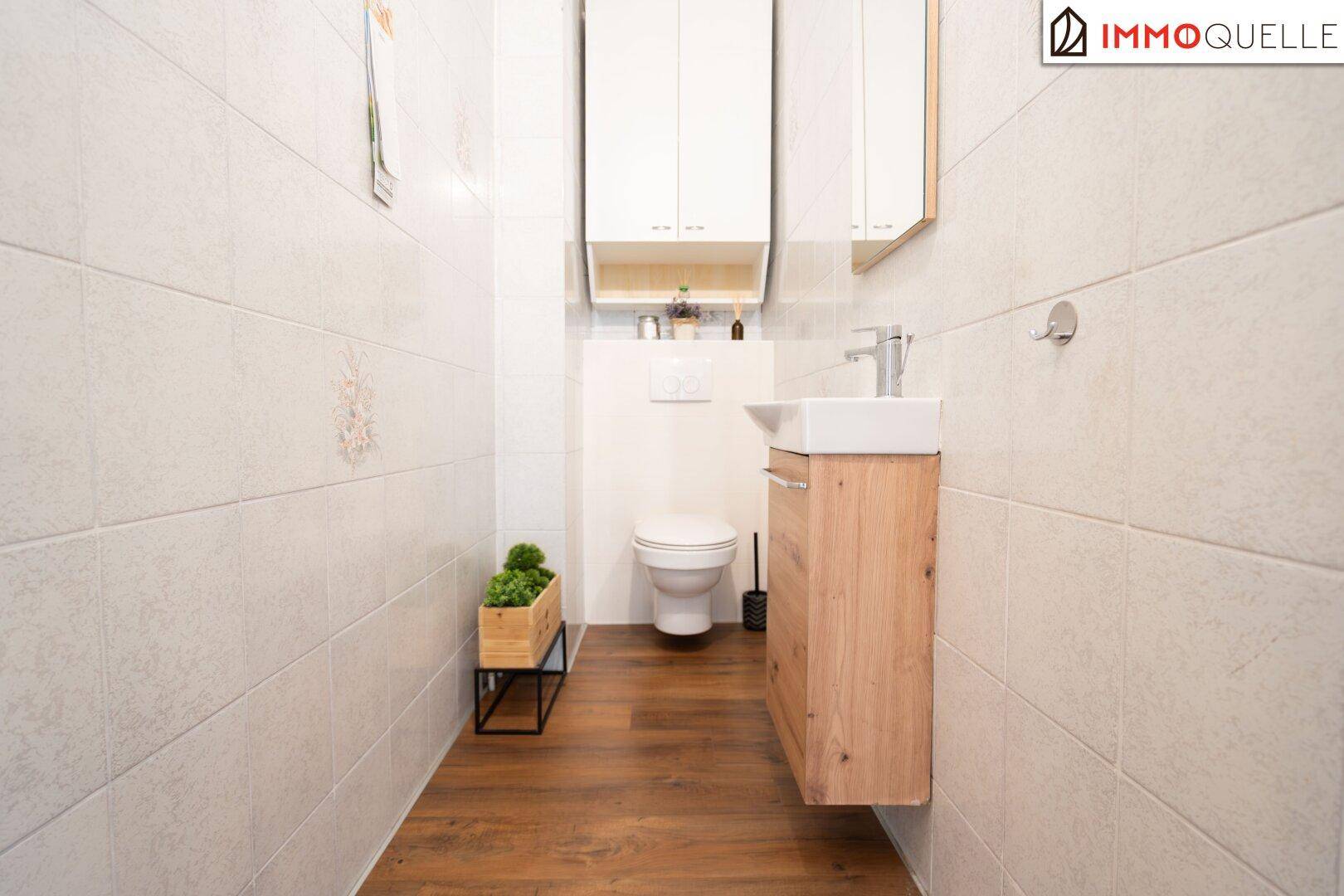Modernes Gäste-WC mit wandhängender Toilette, kleinem Waschbecken und Holzboden.