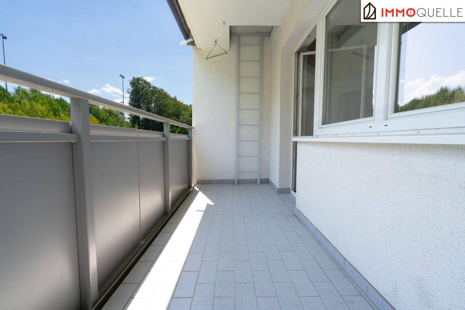 Geräumiger Balkon mit Fliesenboden und Metallgeländer, bietet einen schönen Blick ins Grüne.