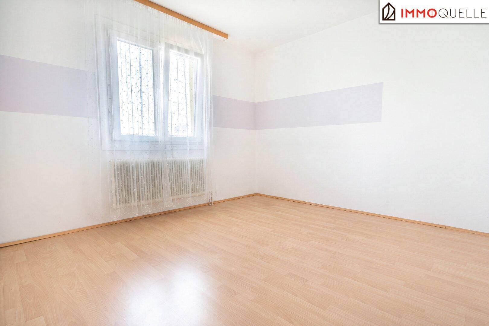 Leeres Zimmer mit hellem Holzboden und einer dezenten lila Streifenwand.