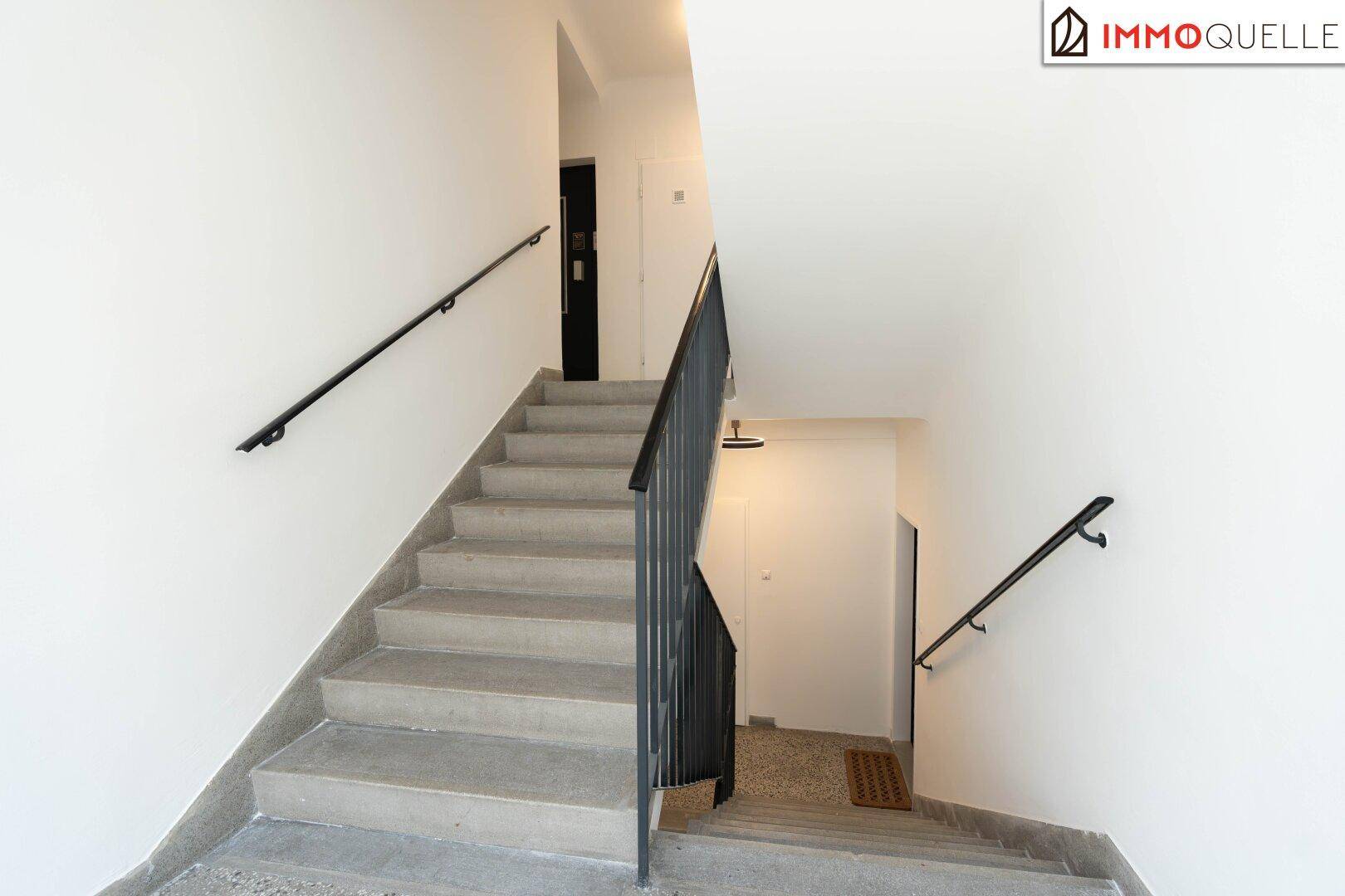 Geräumiges Treppenhaus mit Betonstufen und schwarzem Metallgeländer in einem Mehrfamilienhaus.