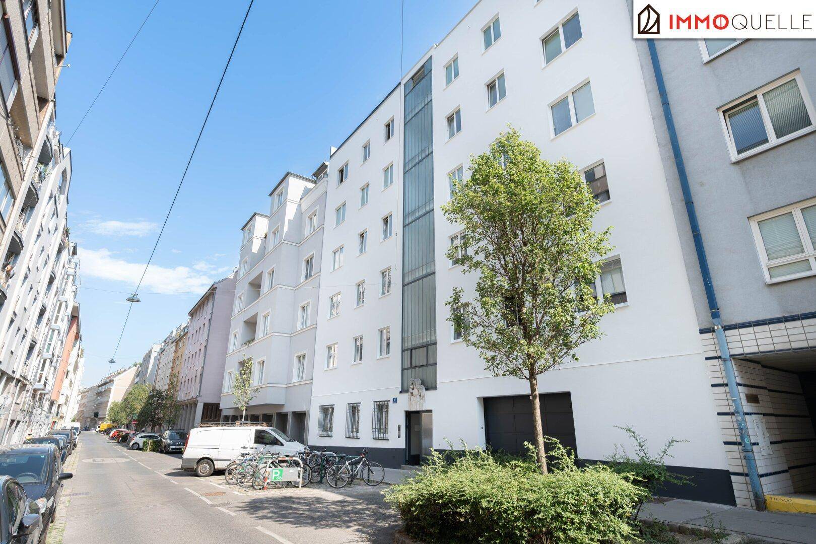 Straßenansicht eines modernen Wohngebäudes mit Baum und parkenden Autos entlang der Straße.