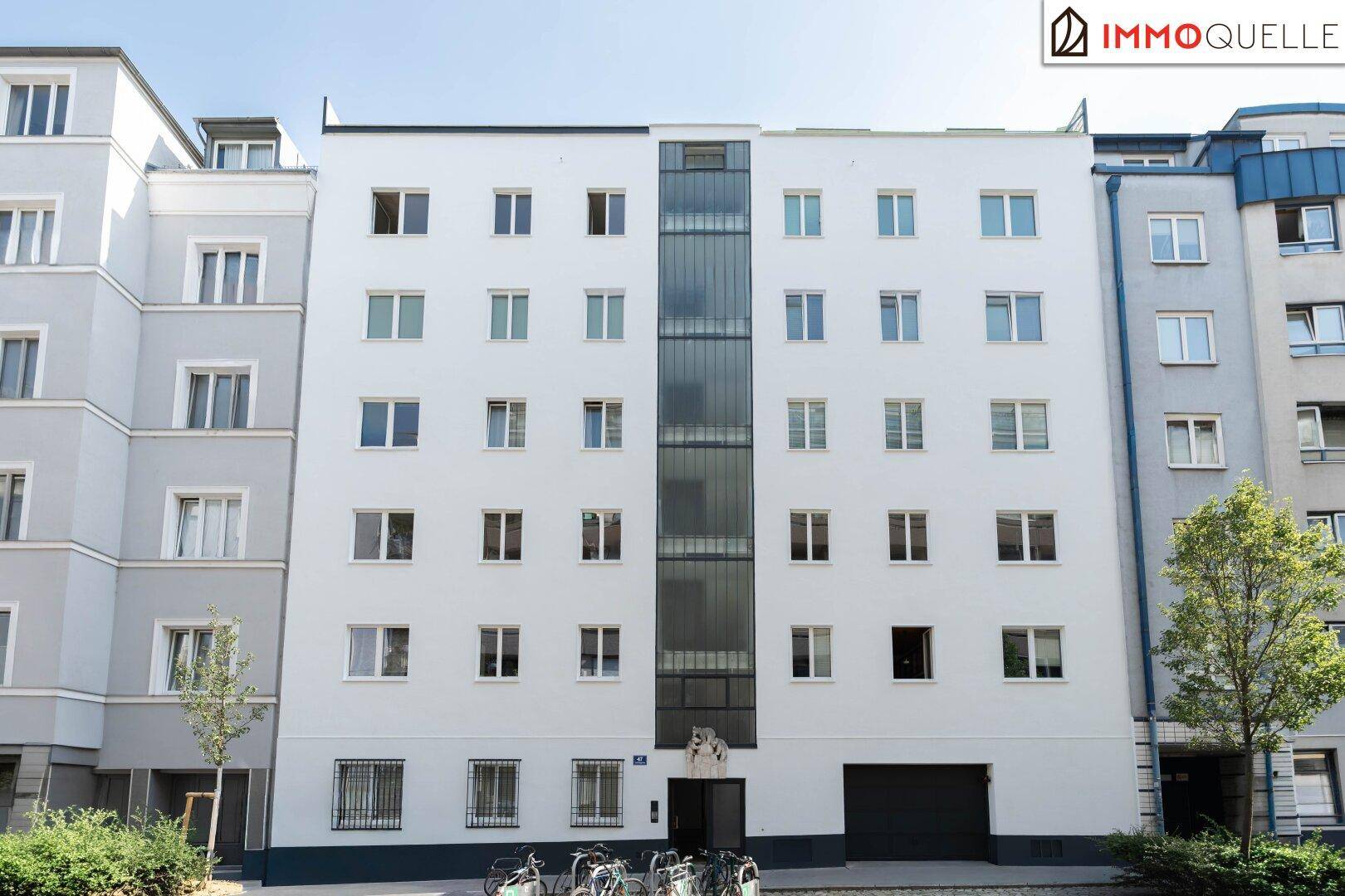 Moderne Wohnhausfassade mit vielen Fenstern, zentraler Glasfront und integrierter Tiefgarage.