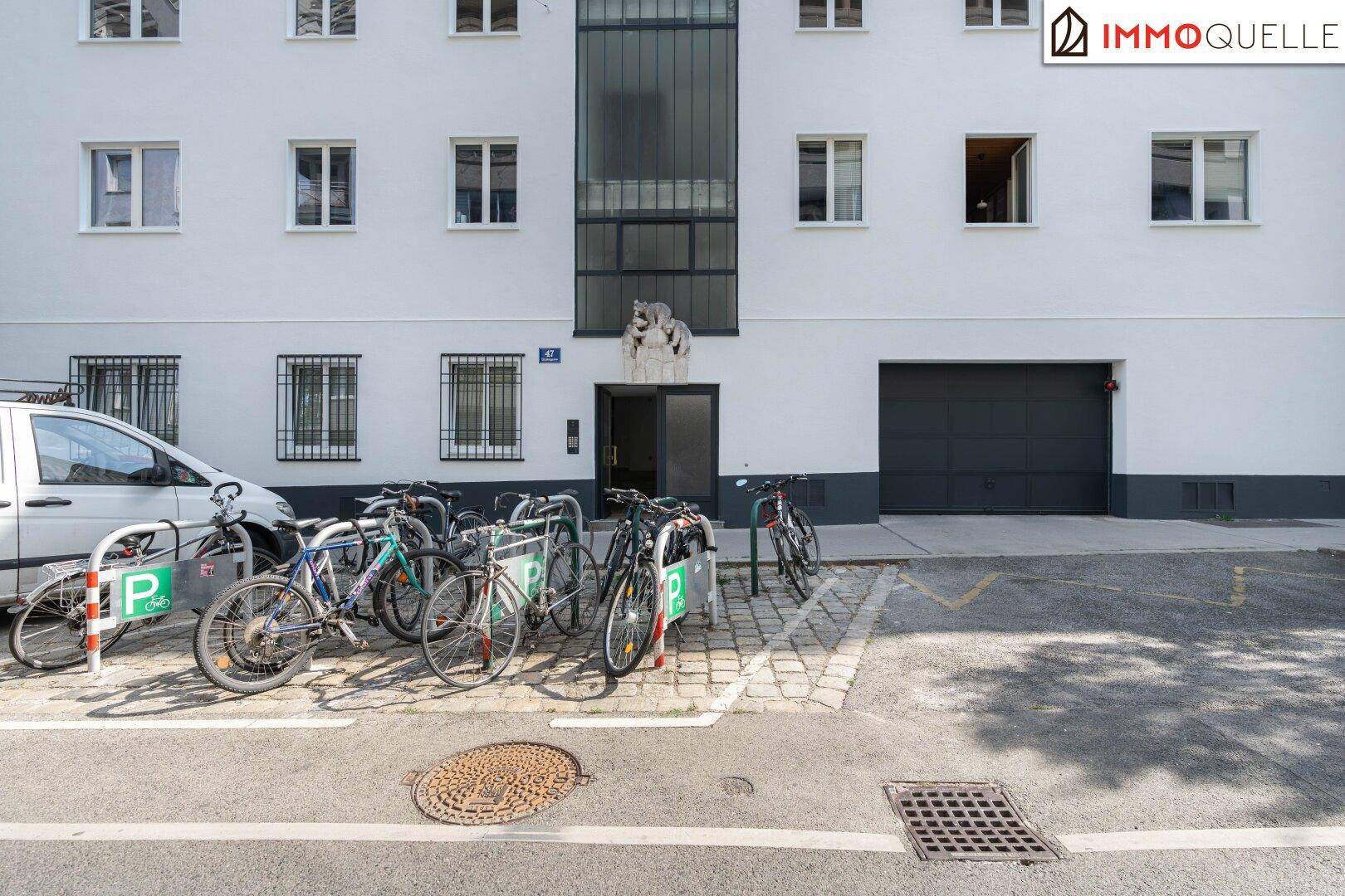 Gebäudefassade mit Eingangsbereich, Garagentor und Fahrradstellplätzen im Vordergrund.