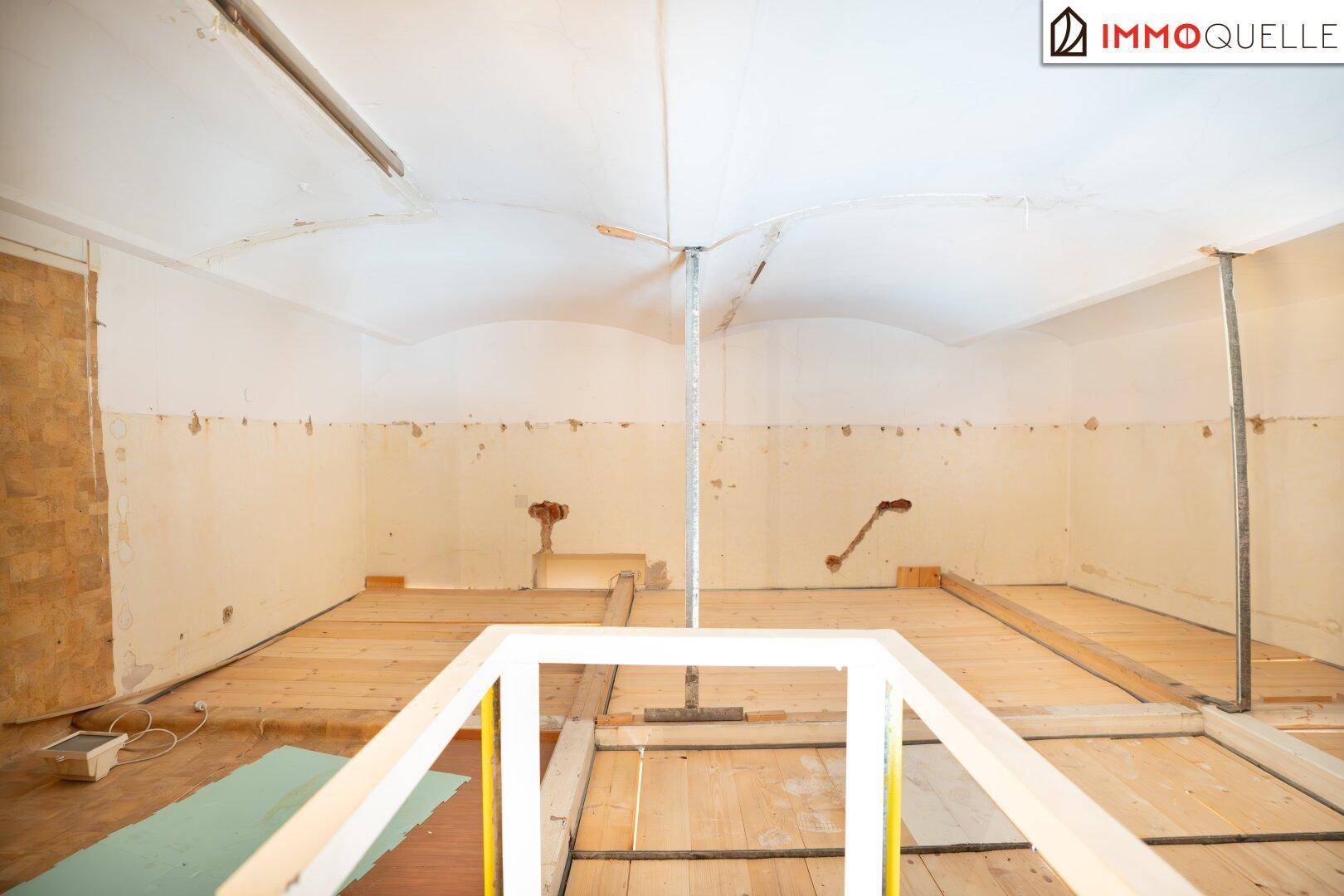 Raum im Rohbauzustand mit freiliegenden Holzdielen, unverputzten Wänden und einer gewölbten Decke.