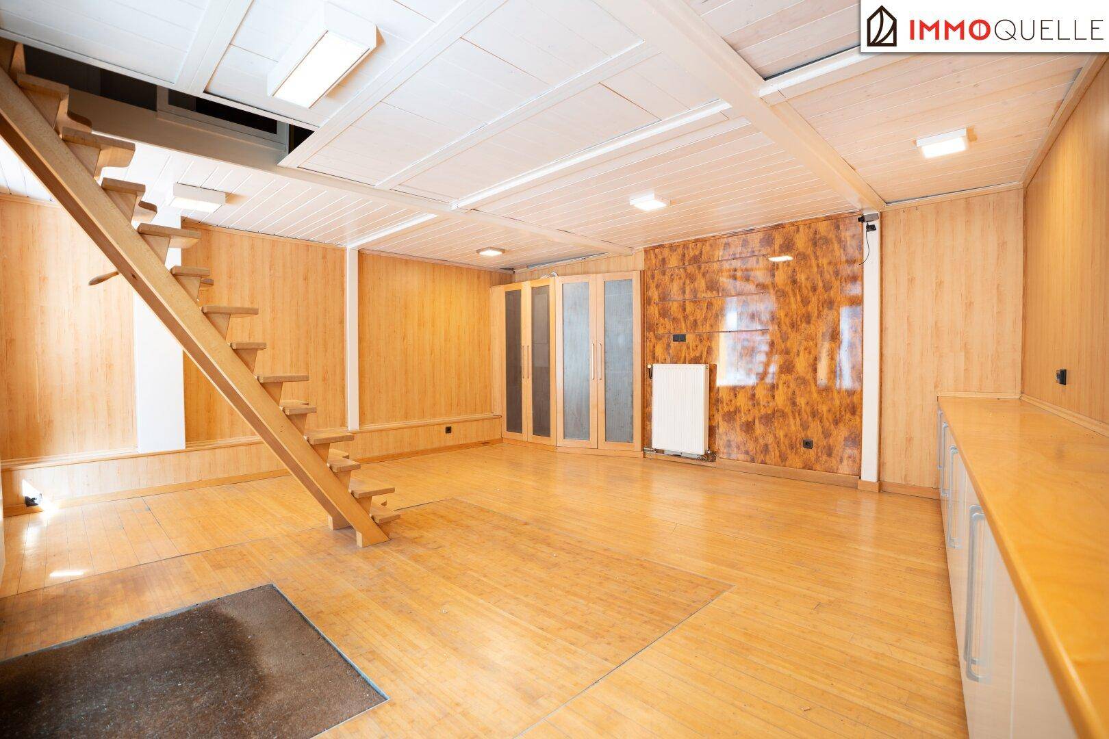 Heller Innenraum mit durchgehender Holzverkleidung, Holzboden und einer freistehenden Holztreppe.