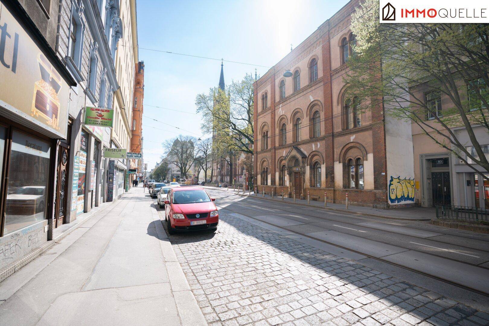 Sonniger Straßenblick mit Kopfsteinpflaster, Straßenbahnschienen und historischen Gebäuden entlang der Straße.