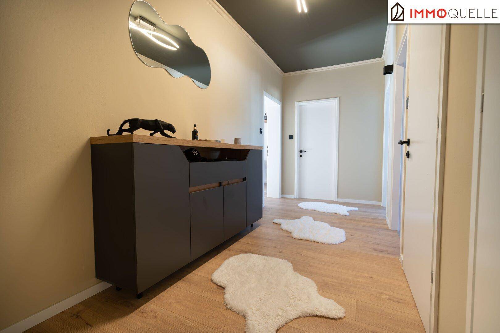 Moderner Flur mit dunklem Sideboard, Spiegel und hellem Laminatboden.