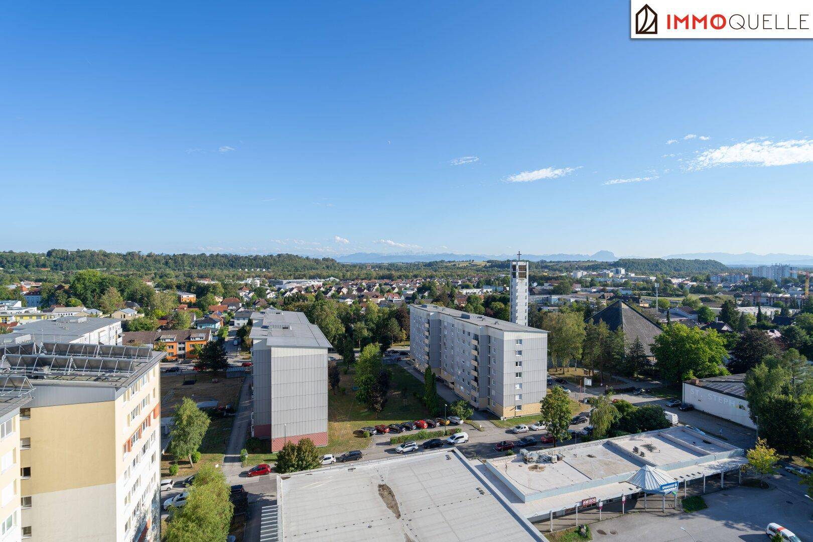 Panoramablick über die Stadt mit Wohngebäuden, Grünflächen und Bergen im Hintergrund.