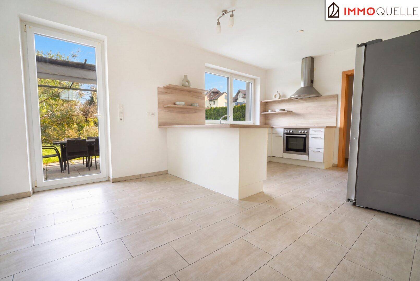 Moderne Küche mit Essbereich, Fliesenboden und direktem Zugang zu einer möblierten Terrasse.