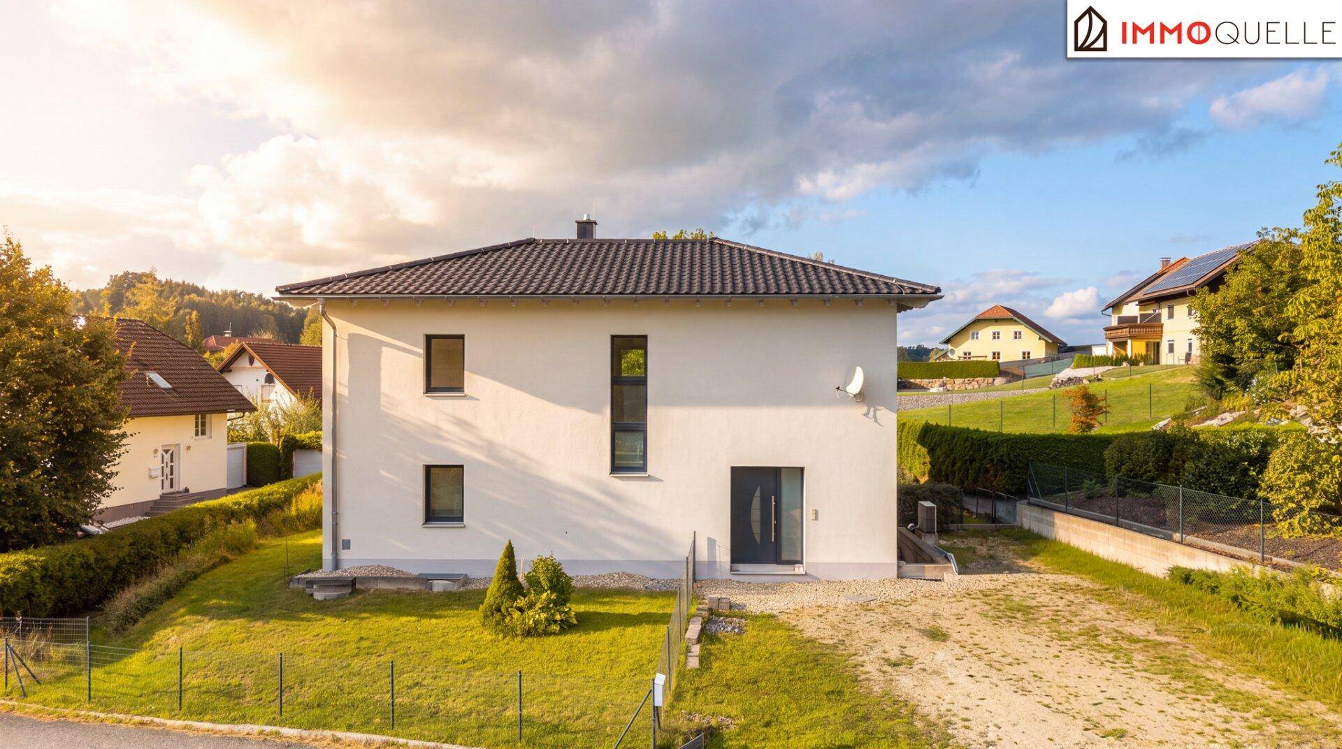 Vorderansicht eines modernen Einfamilienhauses mit heller Fassade und dunklem Satteldach.
