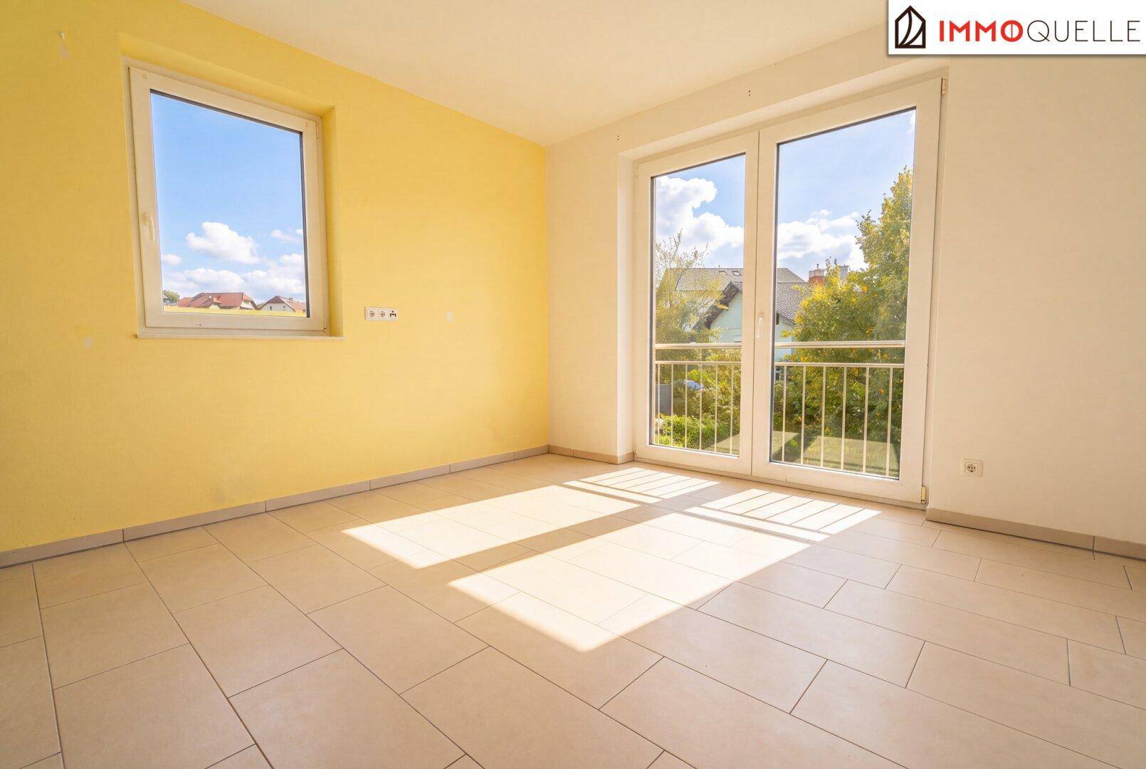 Leeres Schlafzimmer mit Fliesenboden, viel Sonnenlicht und französischem Balkon.