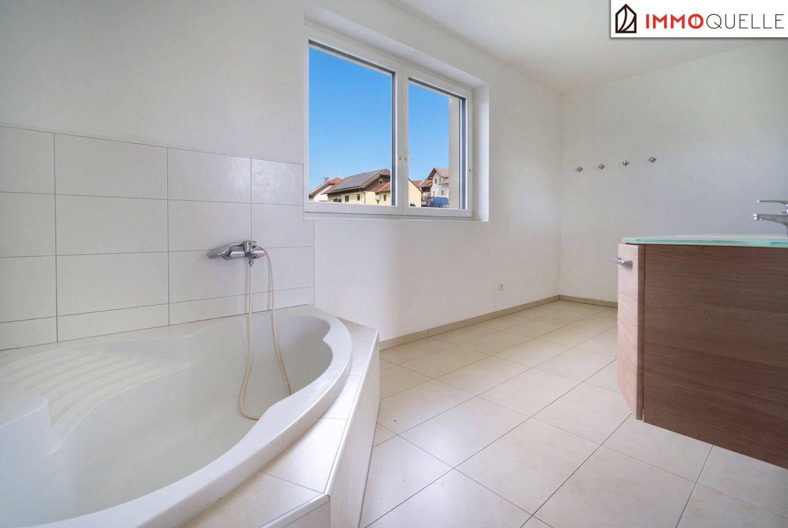 Geräumiges Badezimmer mit Badewanne, Fliesenboden und Fenster für Tageslicht.