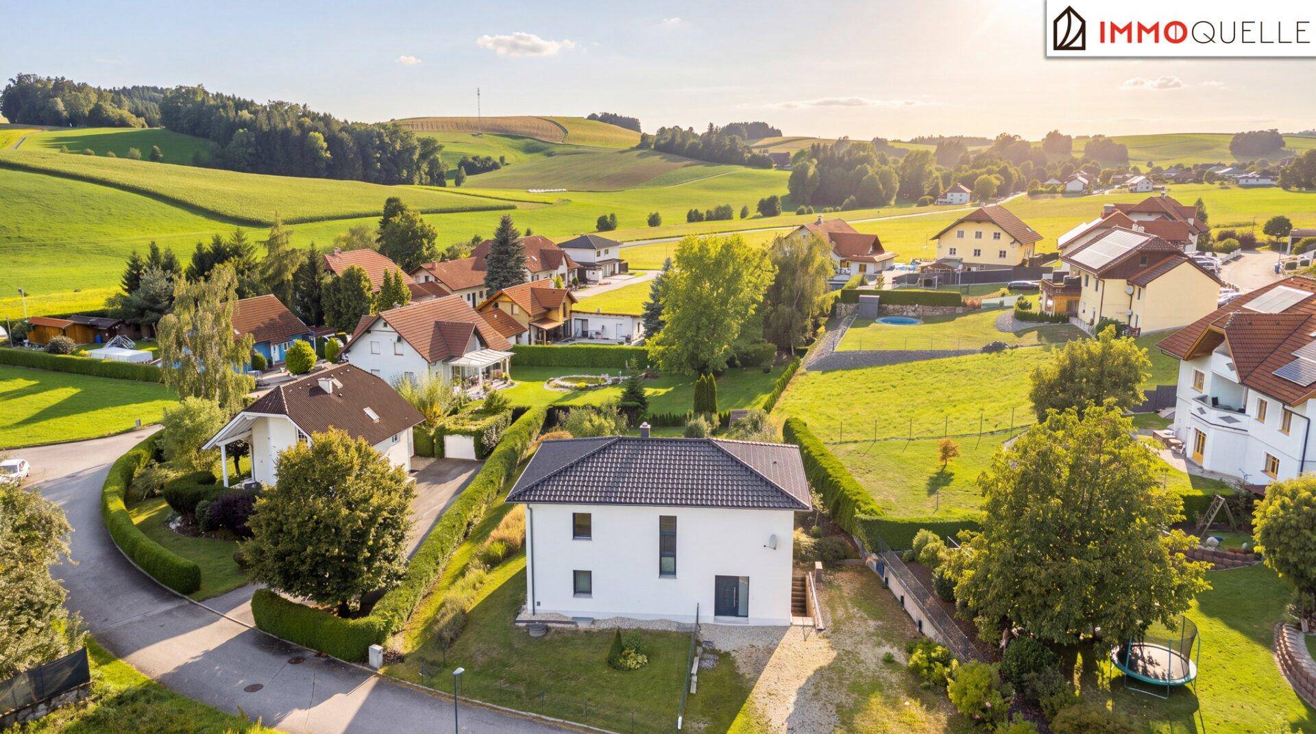 Luftaufnahme einer Wohnsiedlung mit Einfamilienhäusern und grüner Hügellandschaft im Hintergrund.