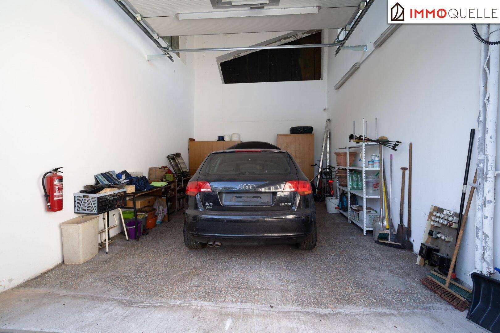 Garage mit einem geparkten Auto, Regalen und Werkzeugen, bietet Stauraum und Arbeitsfläche.