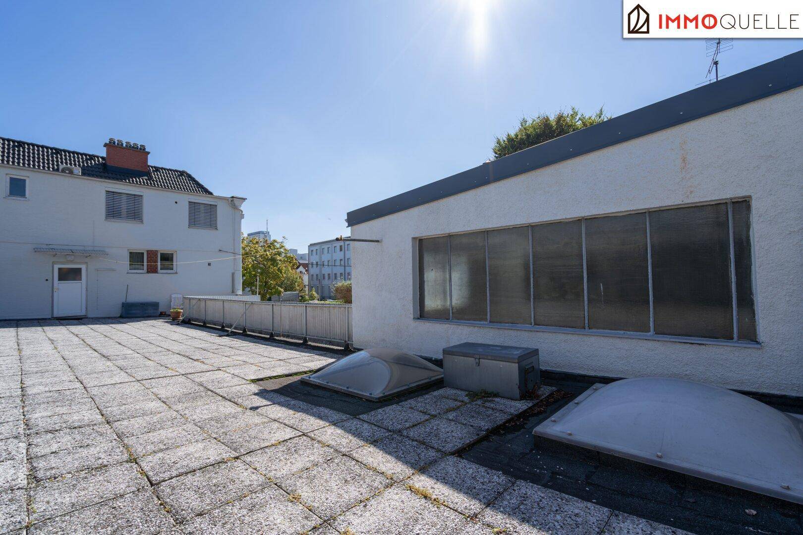 Große, gepflasterte Dachterrasse mit Blick auf die umliegenden Gebäude unter strahlendem Sonnenschein.