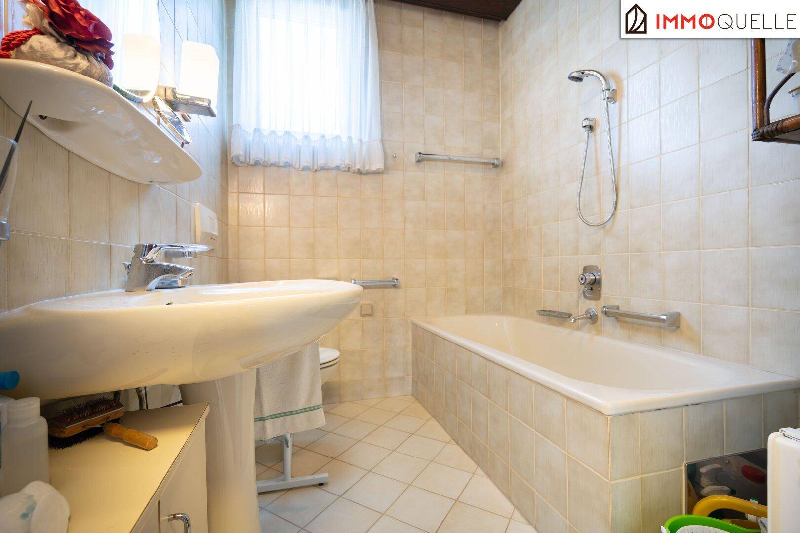 Helles Badezimmer mit Badewanne, Waschbecken und beigefarbenen Fliesen im traditionellen Stil.