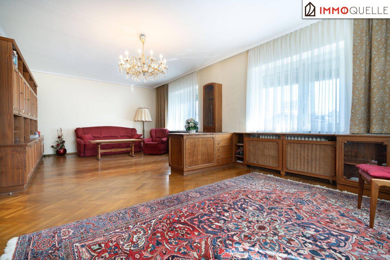 Klassisch eingerichtetes Wohnzimmer mit rotem Sofa, Parkettboden und großem Orientteppich.