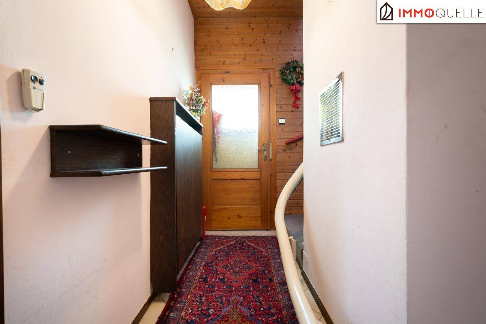 Eingangsbereich mit Holzvertäfelung, Teppichläufer und einer Treppe, die nach oben führt.
