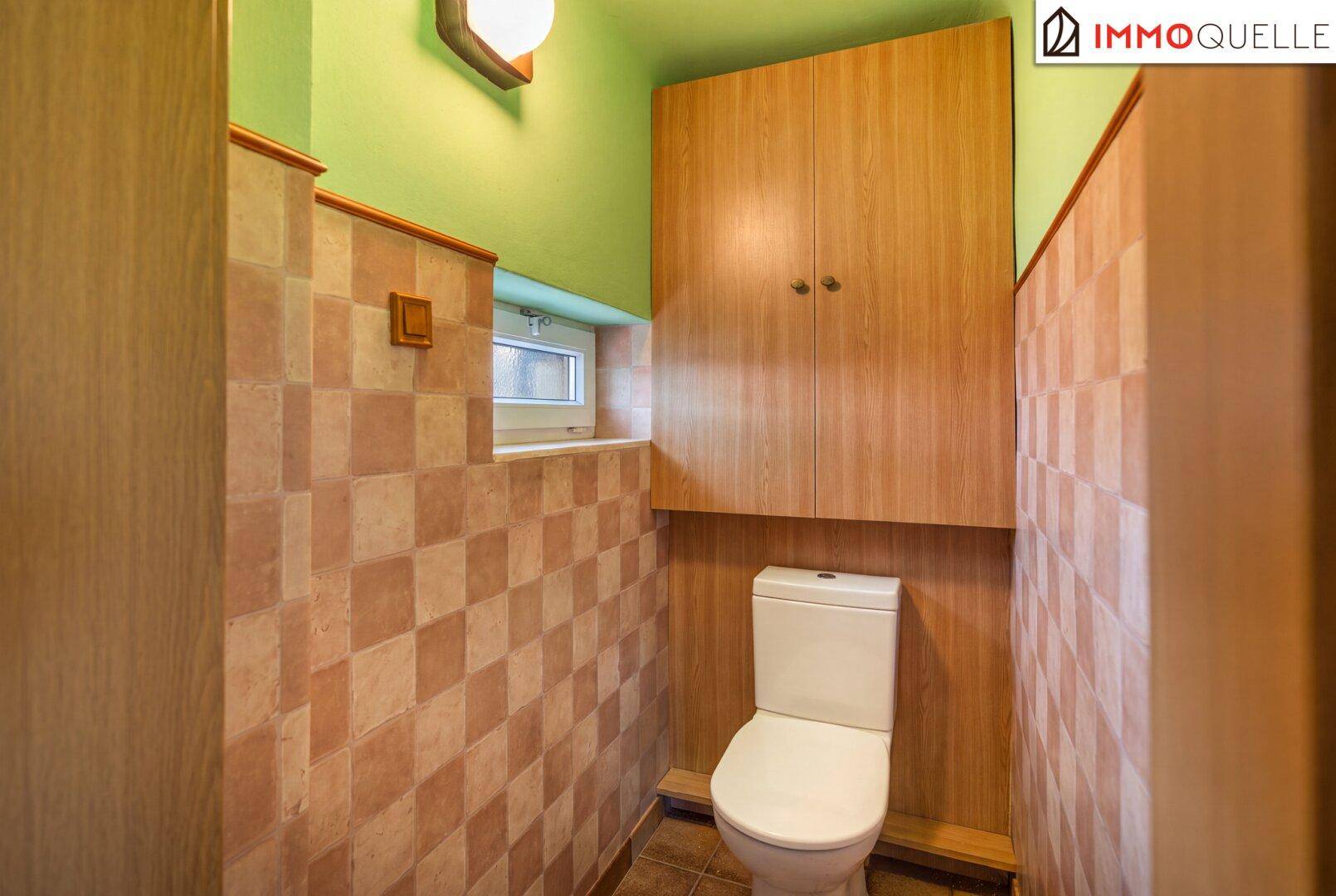 Kleines WC mit gefliesten Wänden, Toilette und einem kleinen Fenster für natürliche Belüftung.