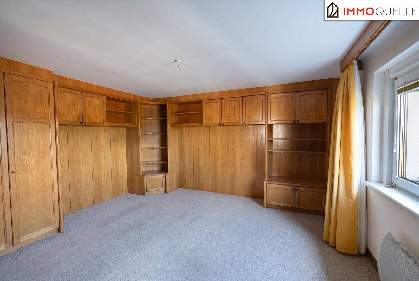 Geräumiges Zimmer mit Teppichboden und umfangreichen Einbauschränken aus Holz entlang der Wand.