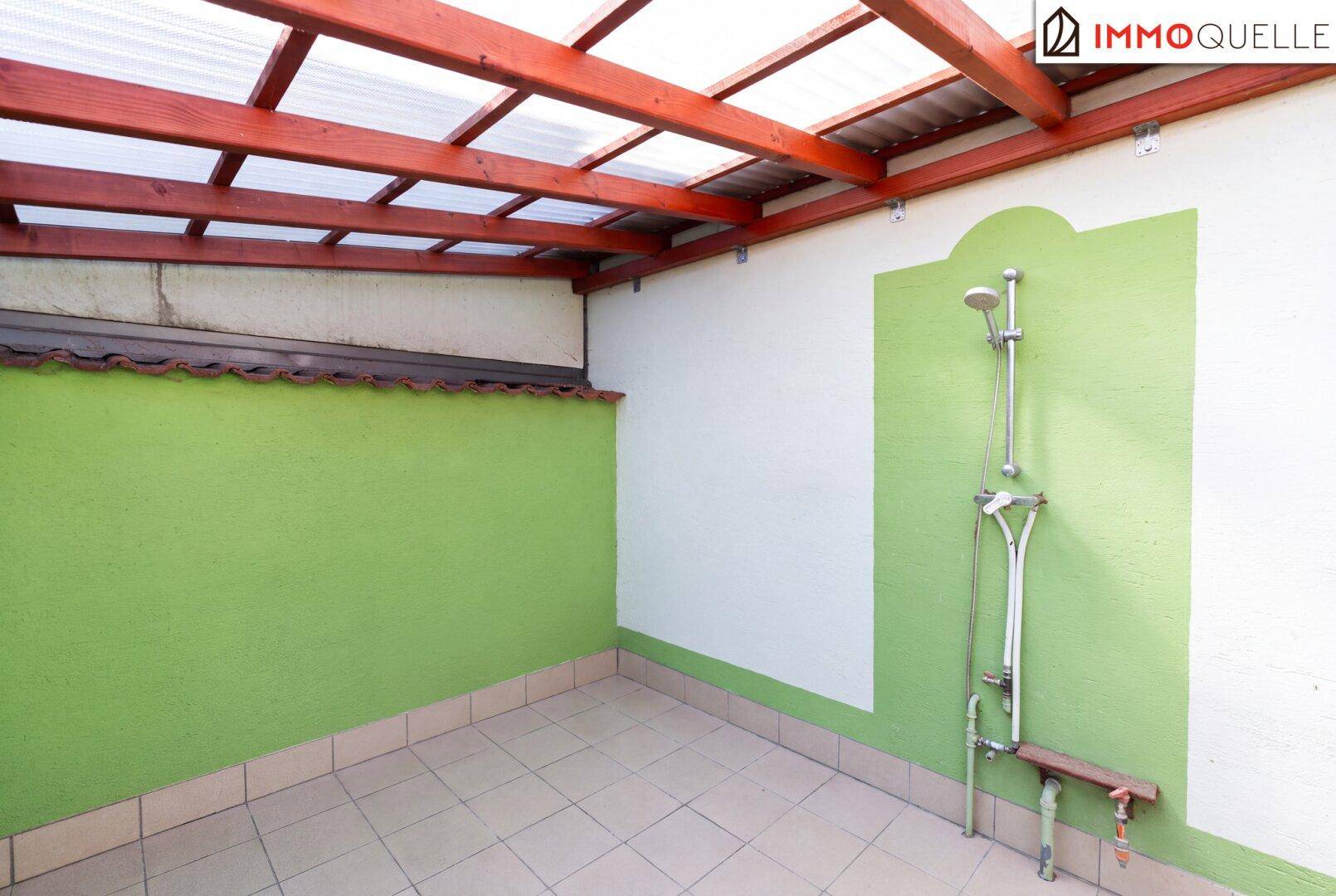 Überdachter Außenbereich mit Dusche und Fliesenboden, ideal für Erfrischung im Sommer.
