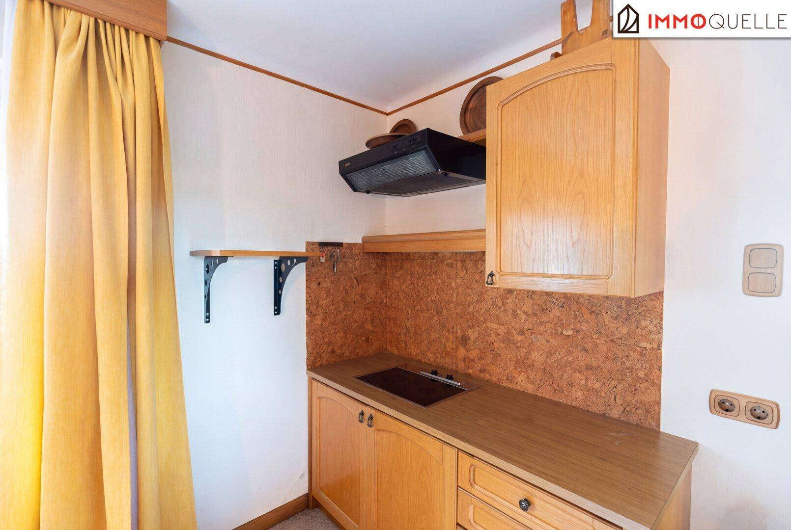 Kleine Küchenzeile mit Holzschränken, Kochfeld und Dunstabzugshaube, ideal für eine kompakte Wohnung.