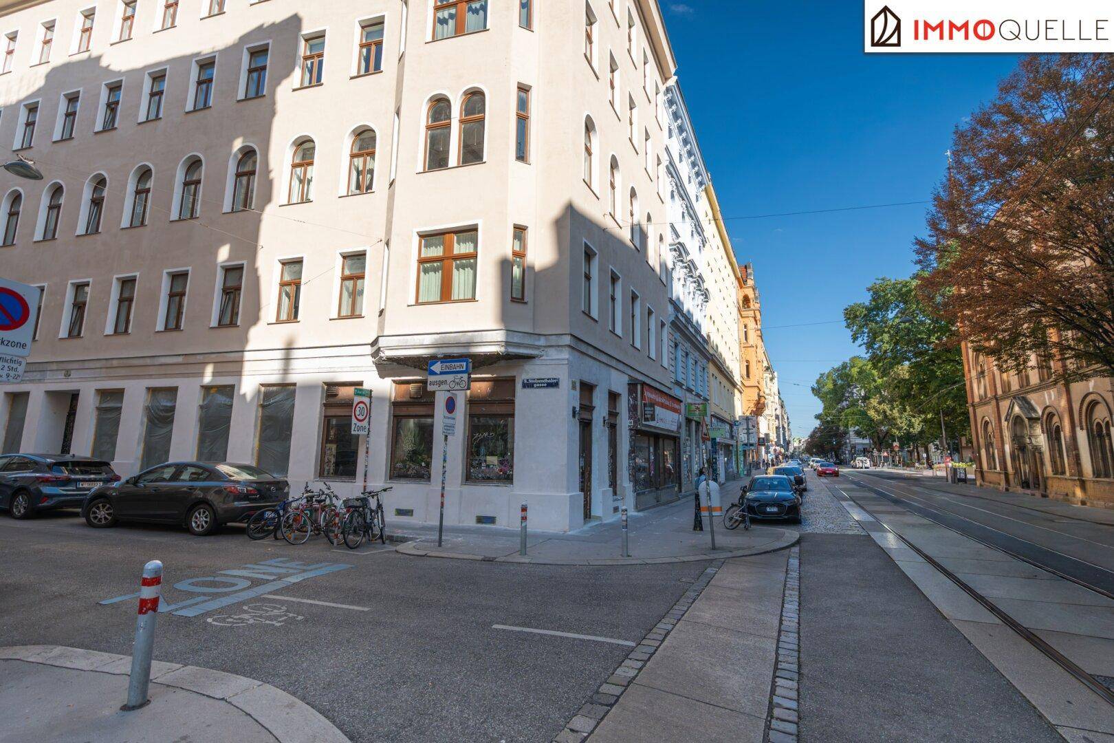 Weitwinkelaufnahme einer Stadtkreuzung mit historischen Gebäuden, geparkten Autos und klarem Himmel.
