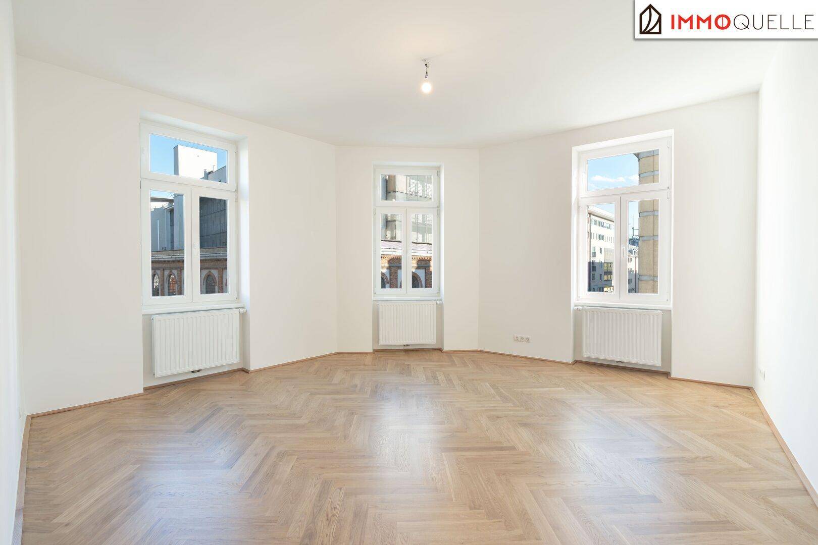 Geräumiges, leeres Wohn- und Esszimmer mit Fischgrätparkett und großen Fenstern.