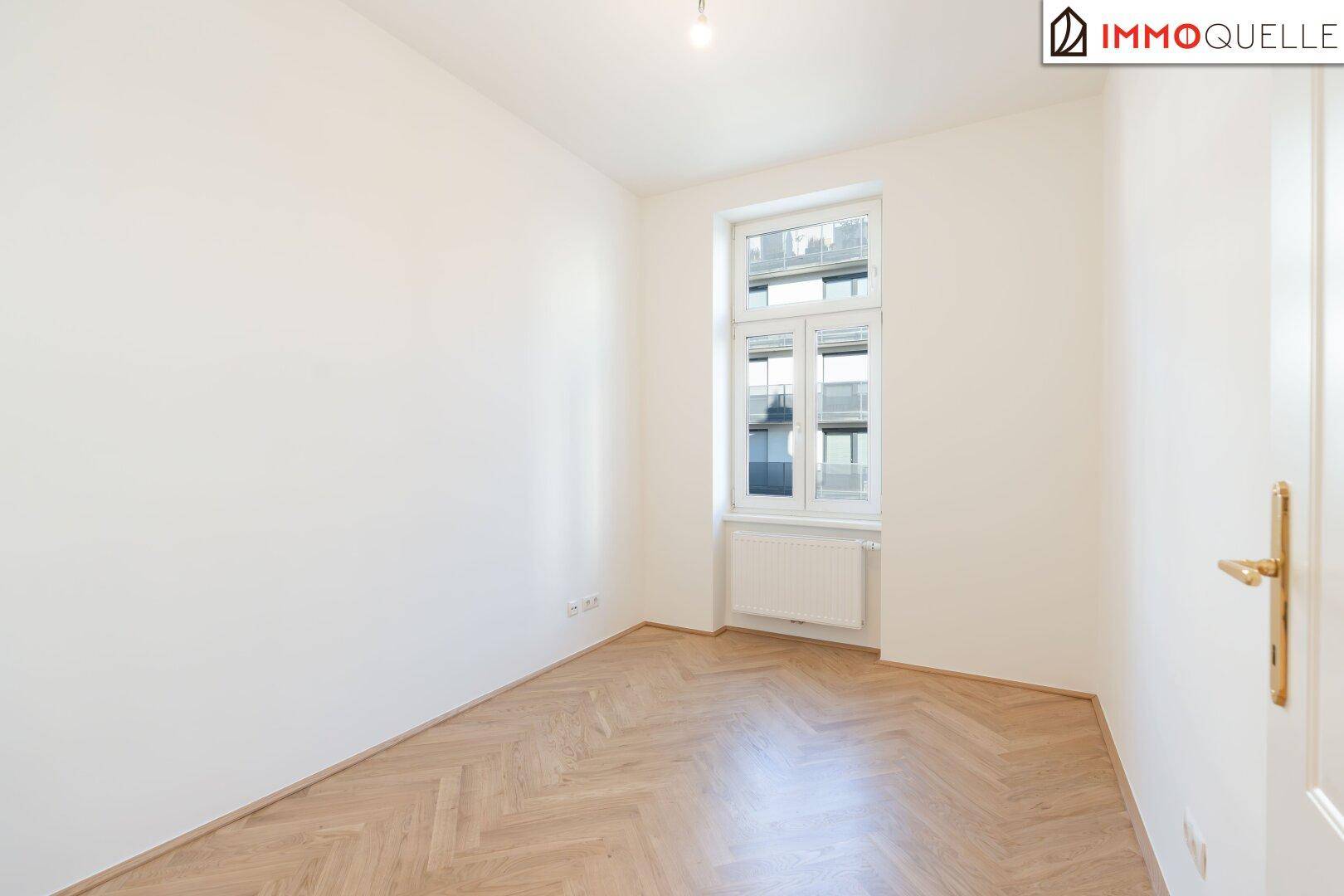 Leeres Zimmer mit Fischgrätparkett und einem Fenster, vielseitig nutzbar als Schlaf- oder Arbeitszimmer.