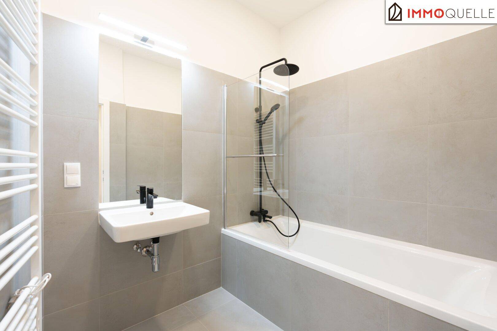 Modernes Badezimmer mit Badewanne, Duschvorrichtung und beheiztem Handtuchhalter, in Grautönen gehalten.