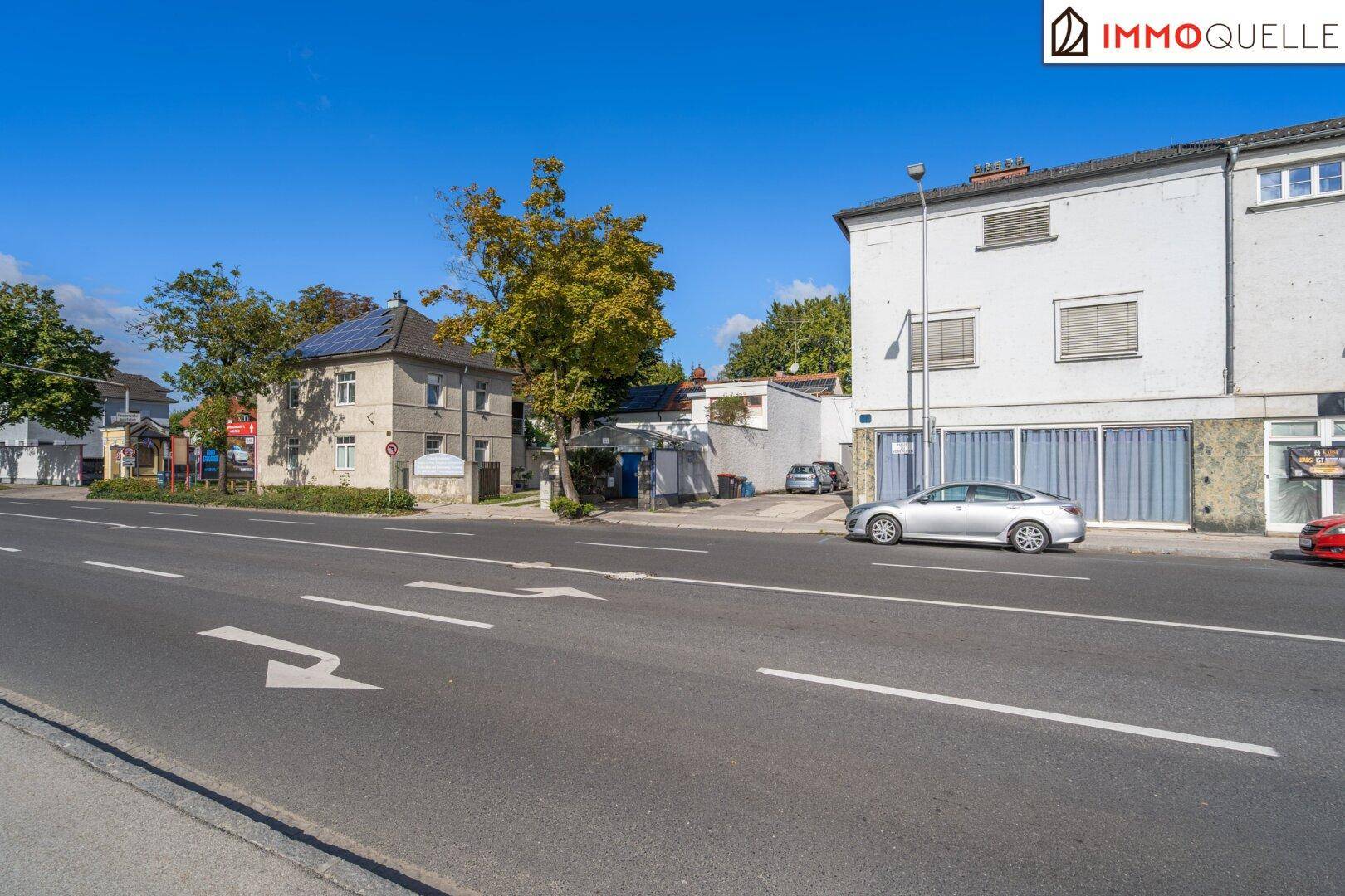 Gesamtansicht des Gebäudes von der Straße mit angrenzenden Häusern und blauem Himmel.