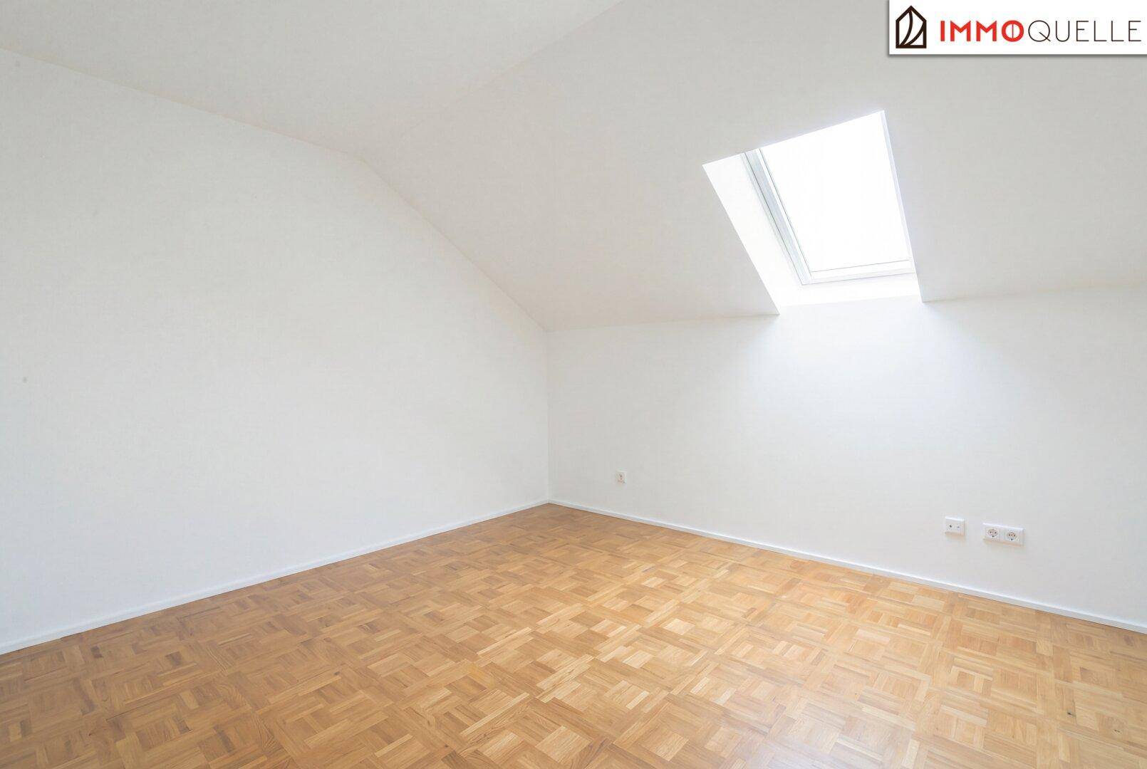 Helles, unmöbliertes Schlafzimmer mit Dachfenster, Parkettboden und schrägen Wänden.