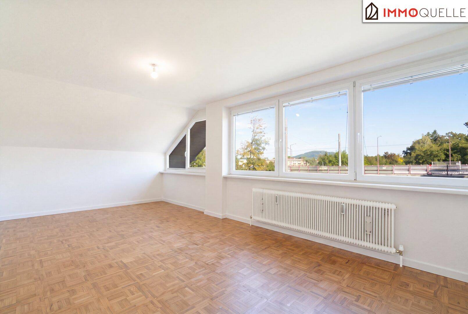 Geräumiger, leerer Wohn-Essbereich mit großen Fenstern, Parkettboden und Dachschrägen.