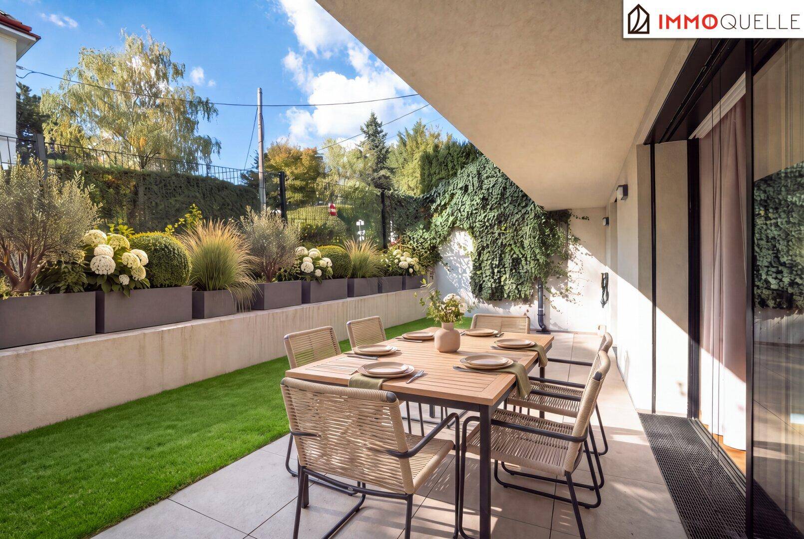 Helle Terrasse mit Esstisch und Stühlen, umgeben von gepflegtem Rasen und üppiger Bepflanzung.