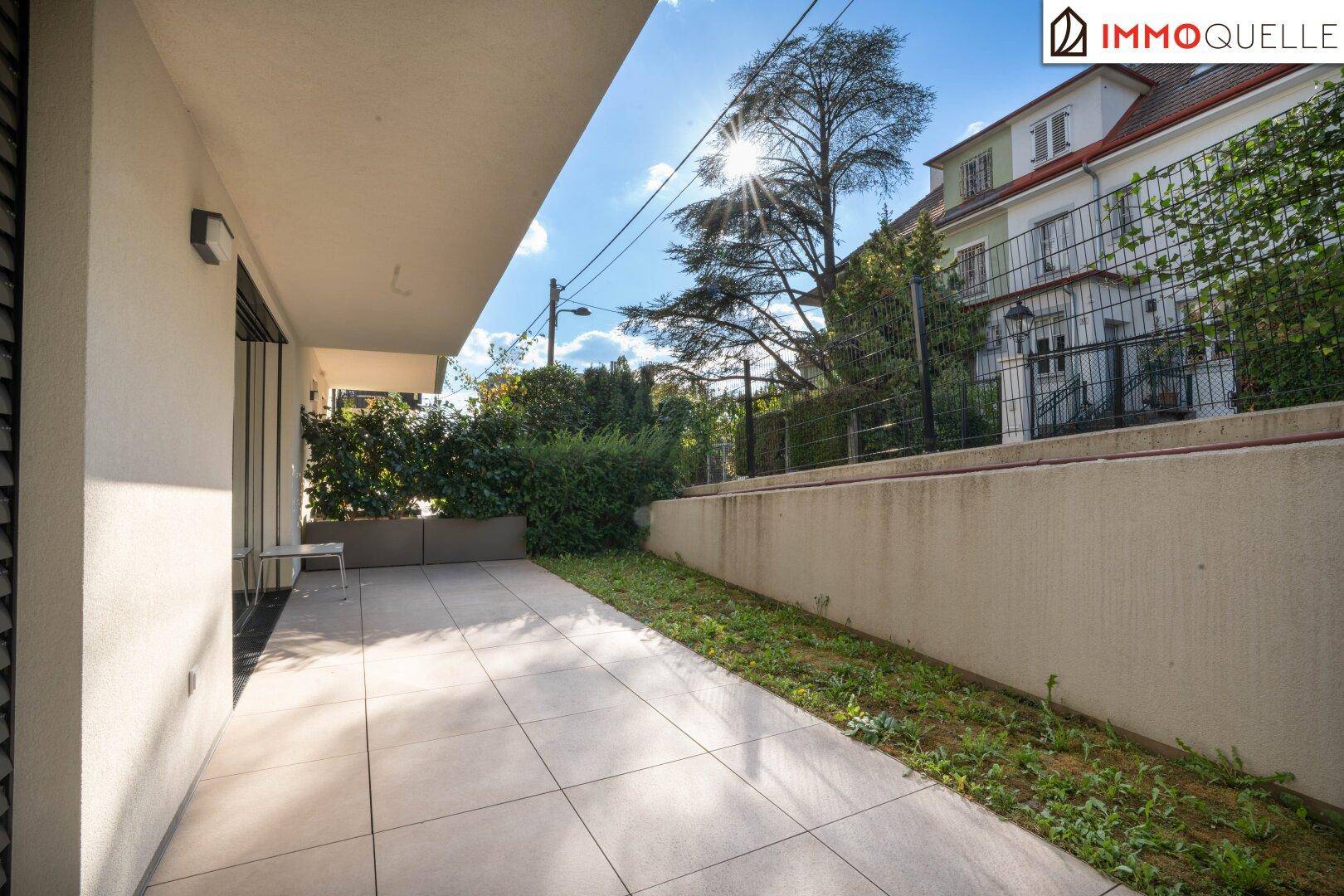 Geräumige, geflieste Terrasse mit angrenzender Grünfläche und Blick auf die umliegenden Gebäude.