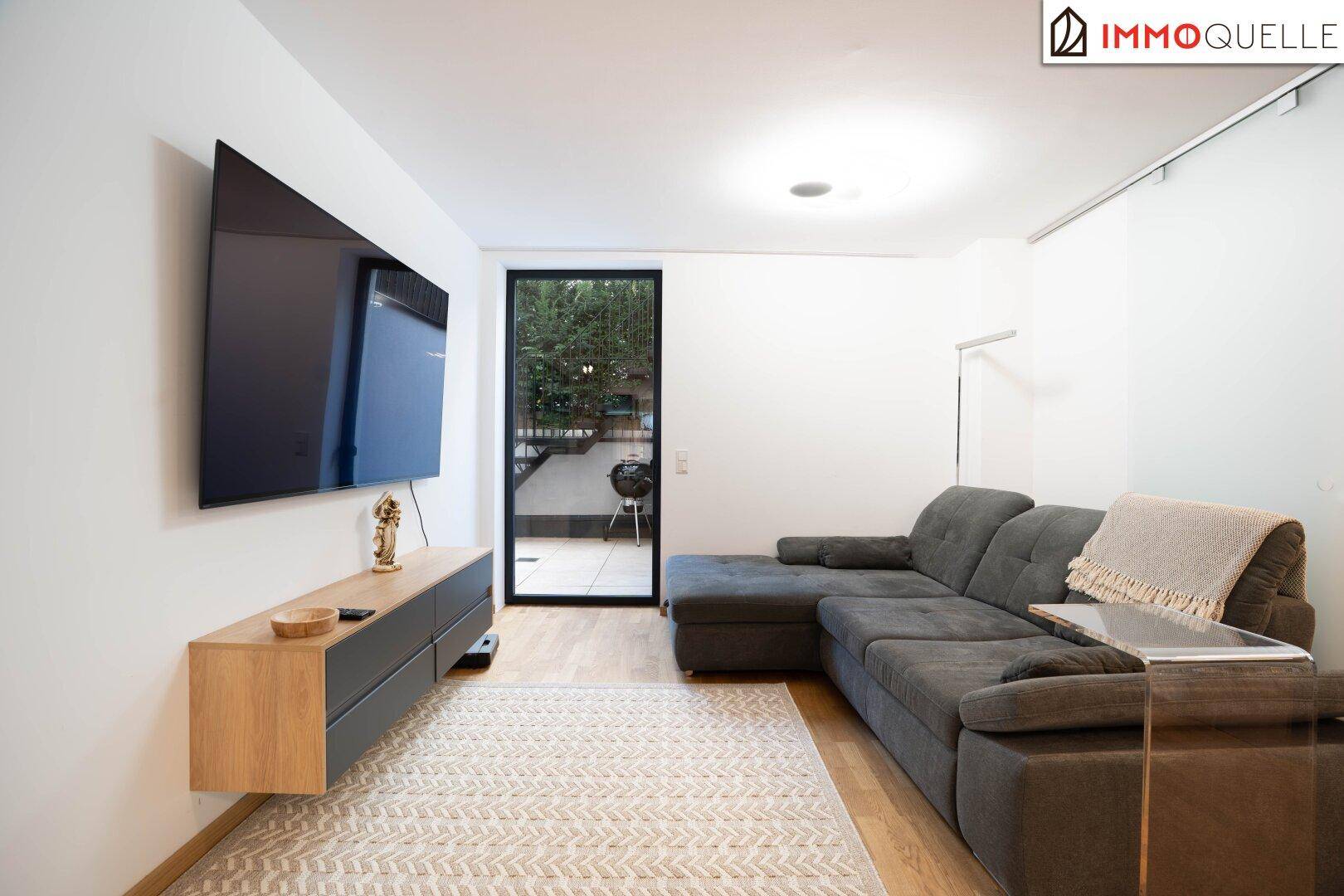 Gemütliches Wohnzimmer mit großem Sofa, Holzboden und Zugang zu einem Außenbereich.