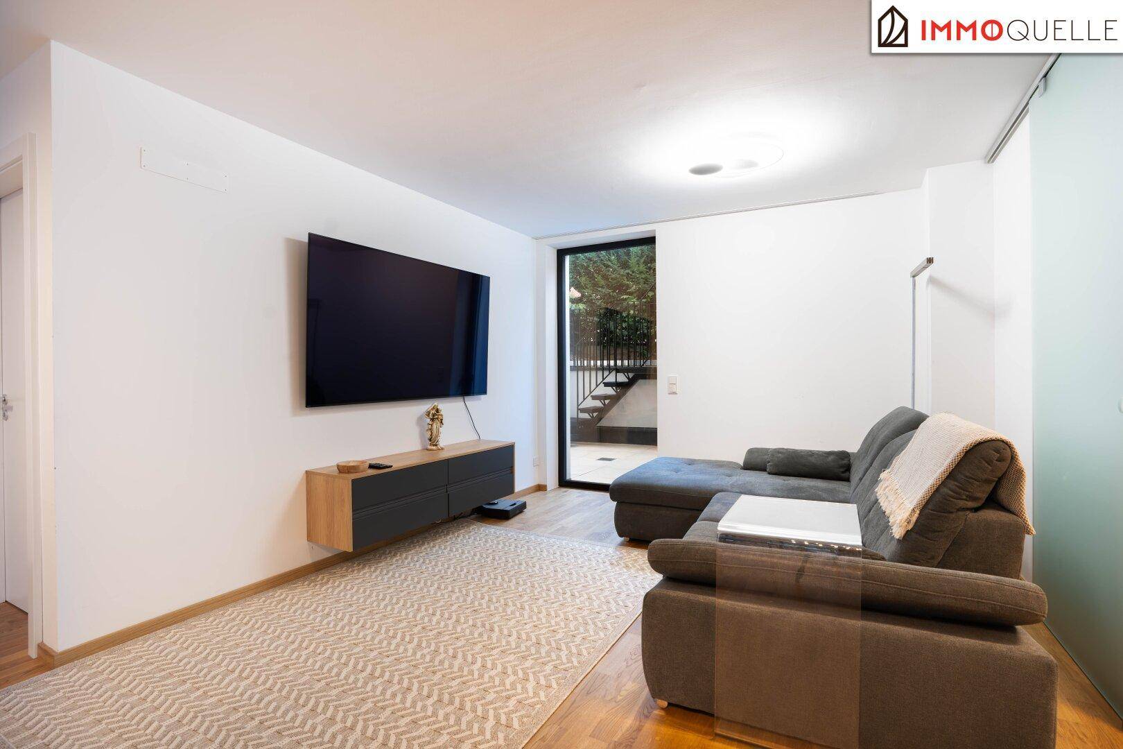 Modernes Wohnzimmer mit bequemer Couch, Holzboden und großem Fernseher an der Wand.