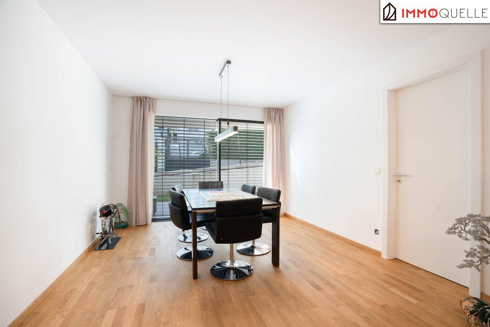 Heller Essbereich mit Holzboden, großem Esstisch und Fenster mit Blick ins Grüne.