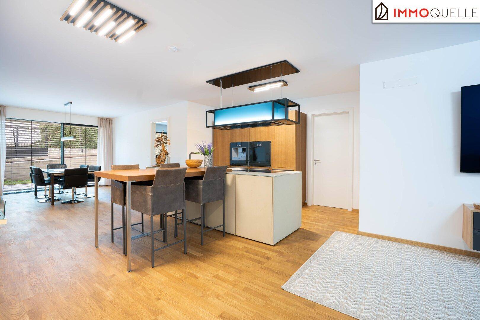 Moderner offener Wohn-Essbereich mit Holzboden, integrierter Küche und Zugang zur Terrasse.