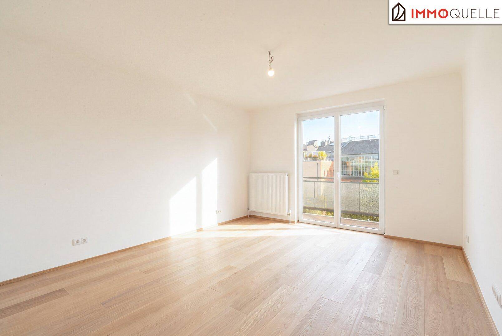 Geräumiges Schlafzimmer mit hellem Parkettboden und direktem Zugang zum Balkon.