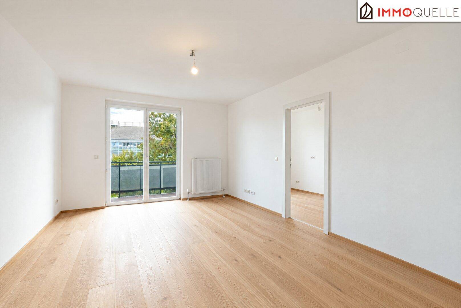 Geräumiges Wohnzimmer mit hellem Holzparkett und direktem Zugang zum Balkon.