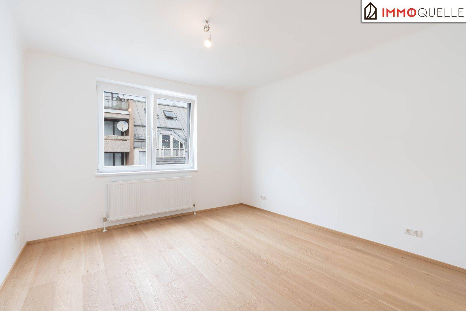 Helles Schlafzimmer mit Parkettboden und großem Fenster für viel Tageslicht.