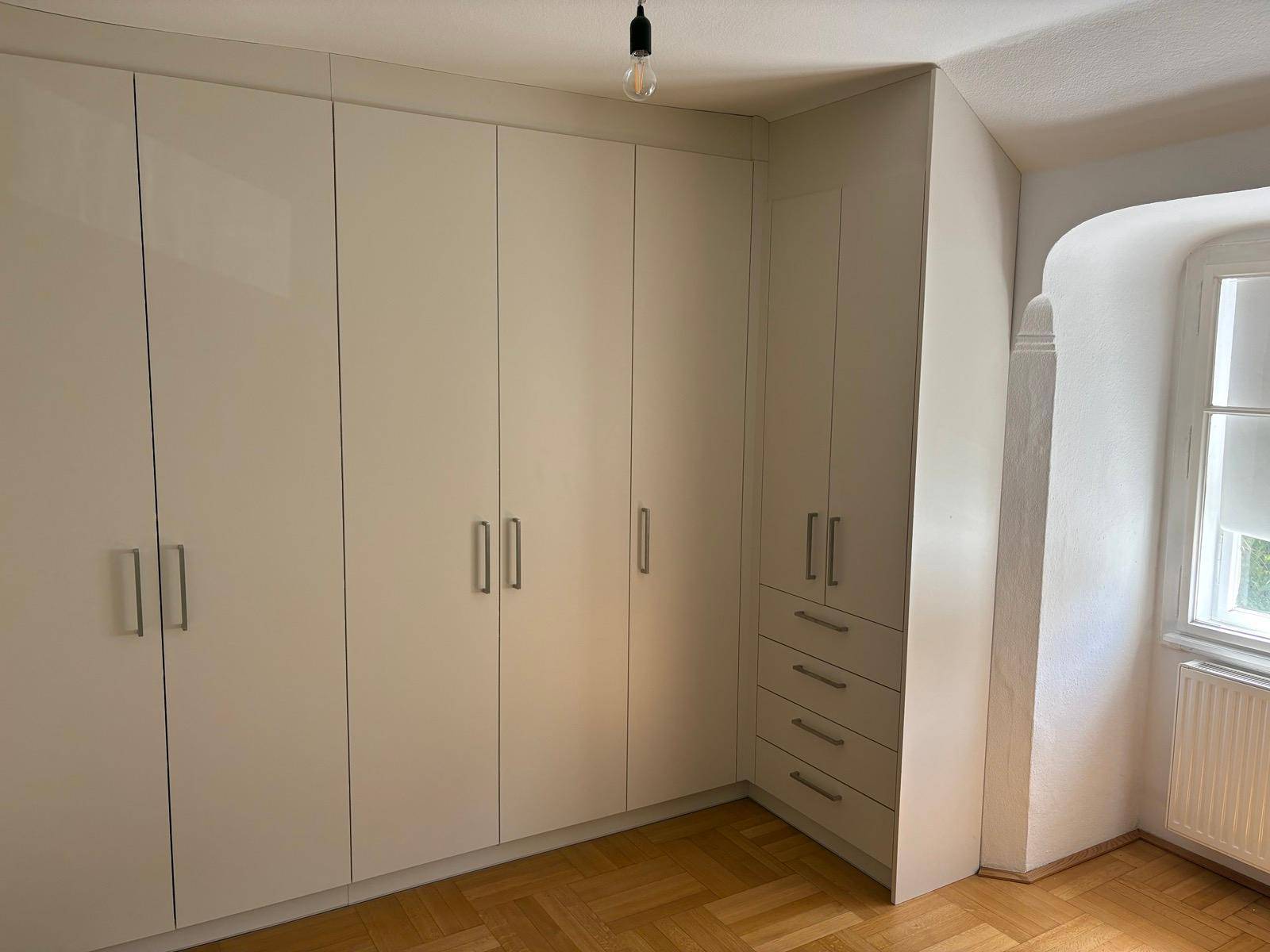 Schlafzimmer mit maßgefertigten weißen Einbauschränken und Parkettboden.