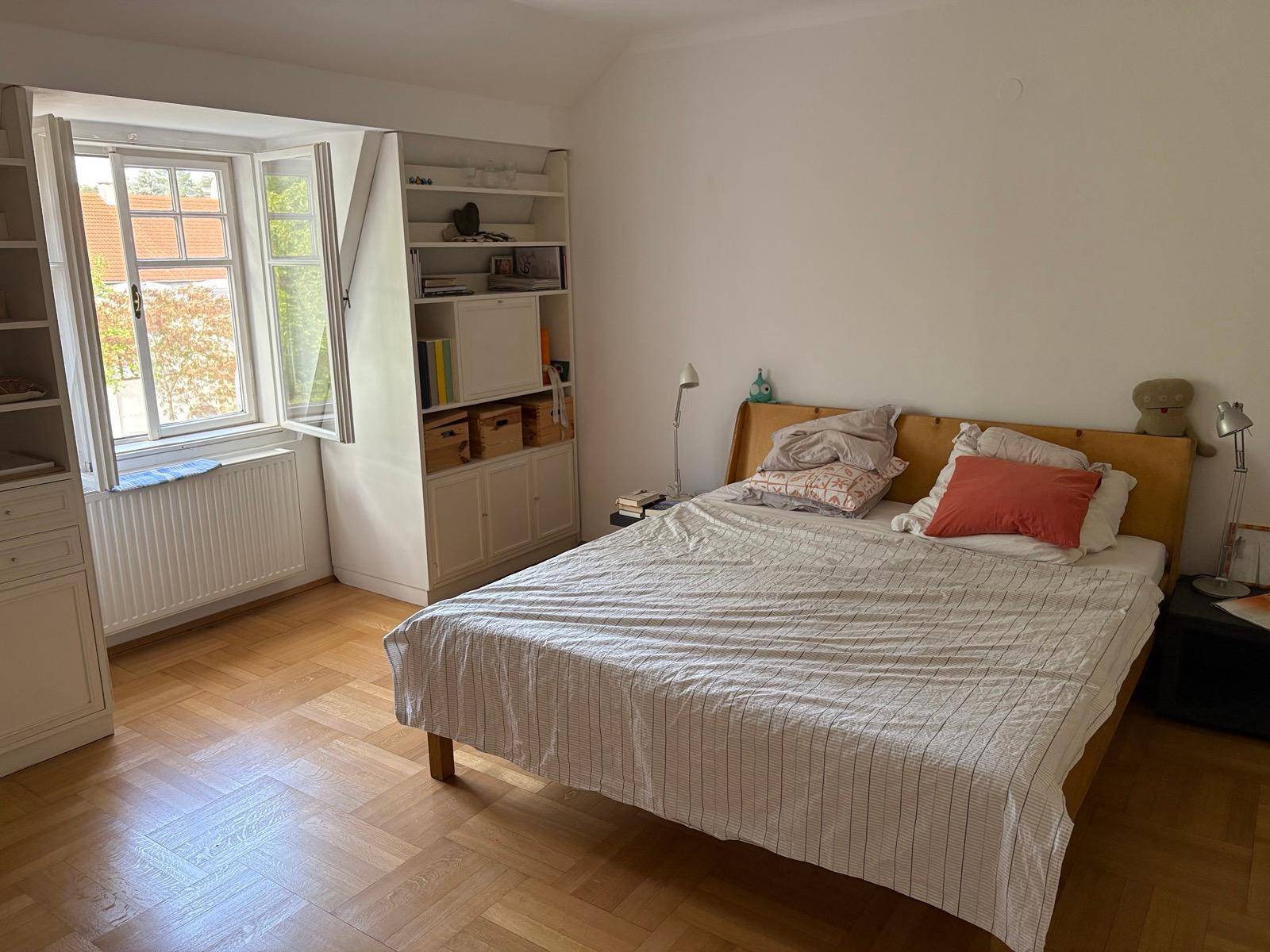 Helles Schlafzimmer mit Doppelbett, Holzparkett und Fenster mit Blick ins Grüne.