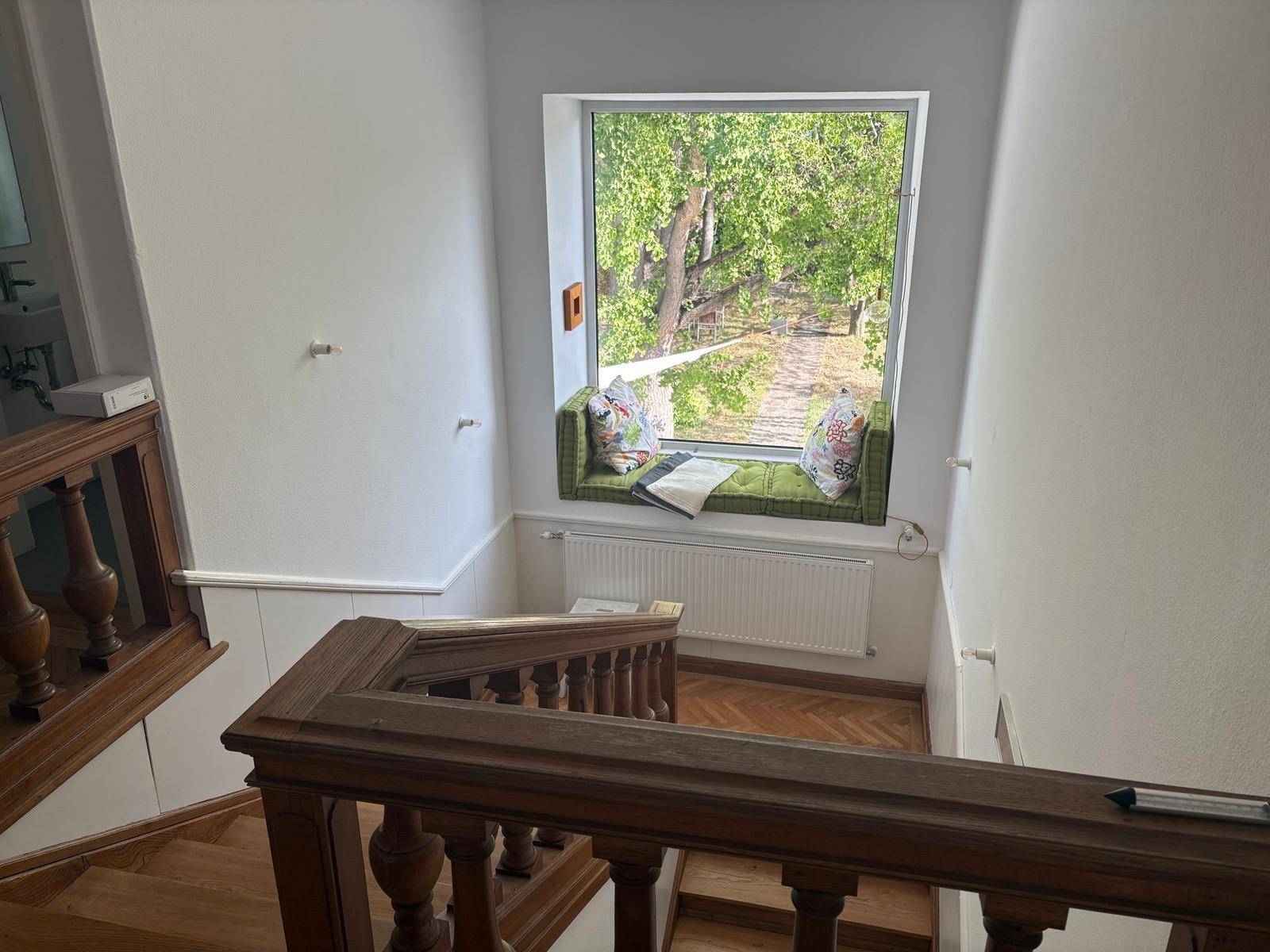 Heller Treppenaufgang mit Holzgeländer und einem gemütlichen Fensterplatz mit Blick ins Grüne.
