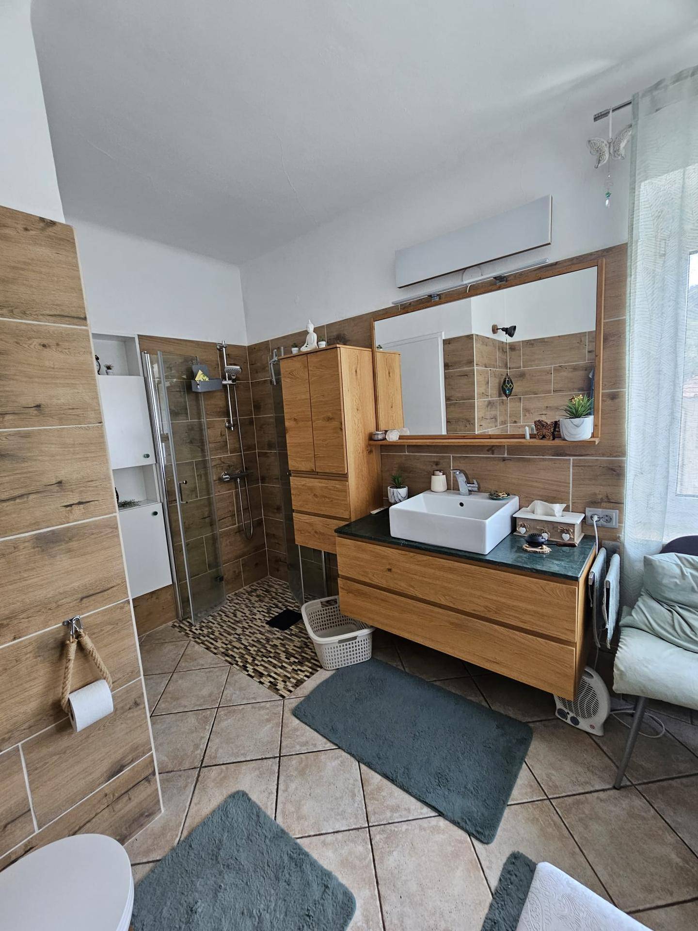 Badezimmer mit Dusche, Holzwaschtisch und großem Spiegel, modern eingerichtet.