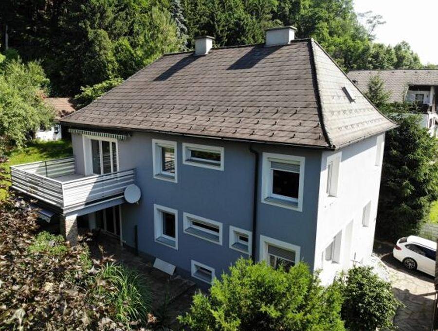 Vogelperspektive des Hauses mit Balkon und umliegender grüner Landschaft unter blauem Himmel.